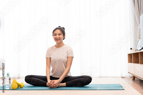 Productive activity concept a girl with a bun sitting on the rectangular green mat stretching her both legs parallel to the floor
