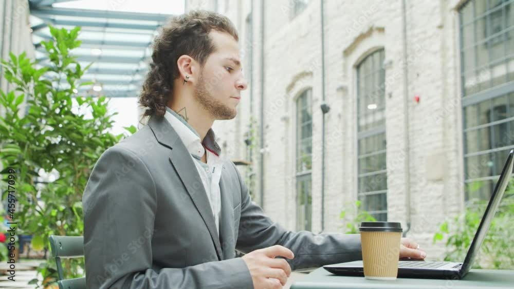 Young successful caucasian businessman works in an outdoor cafe using a computer and a smartphone. Business, freelance and remote work. Young successful caucasian businessman works in an outdoor cafe using a computer and a smartphone. Business, freelance and remote work.
