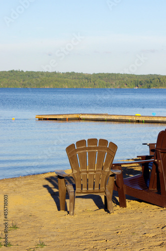 bright yellow Adirondack chair at water’s edge with blue sky copy space