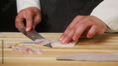 Professional Chef cutting raw white fish close-up, thin slices. Man cooking seafood dishes using sharp knife, wearing apron. Process of preparing ingredients for Peruvian ceviche.  photo