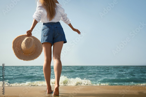 Young woman with straw hat near sea on sunny day in summer, closeup back view