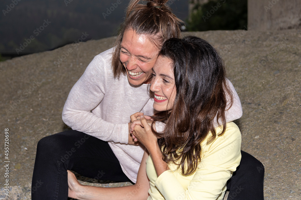 young lesbian couple laughing embracing sitting on a wall young lesbian couple laughing embracing sitting on a wall
