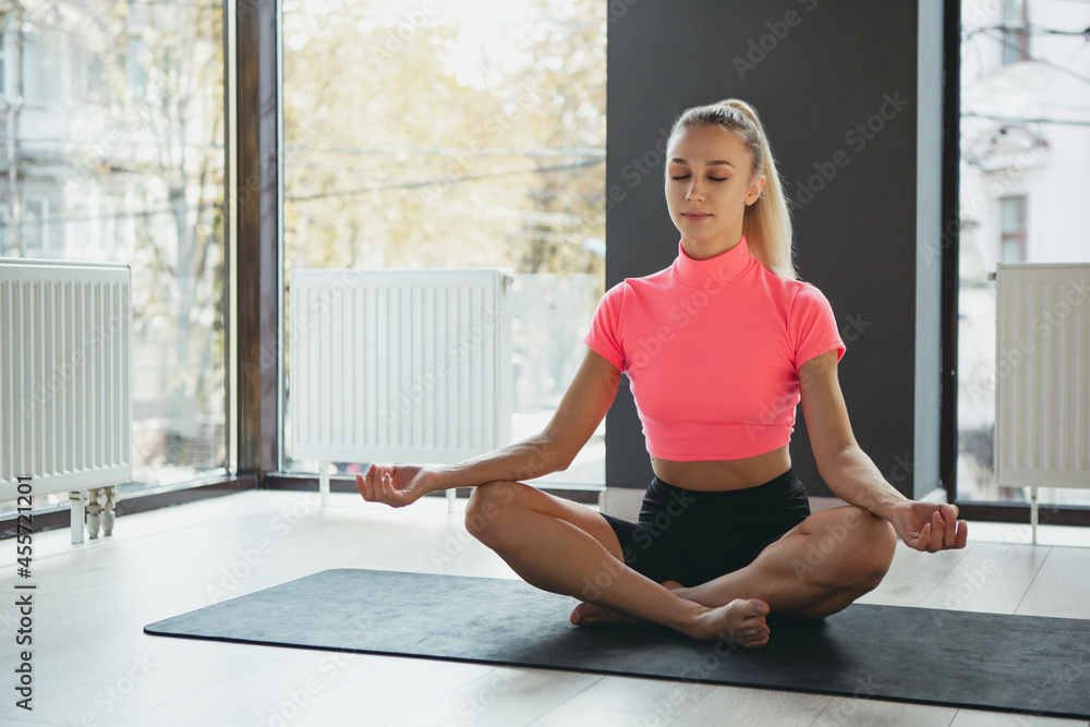 Portrait of young slim sportive woman in sportswear doing yoga exercise on sports mat at yoga meditation center. Concept of healthy lifestyle, wellbeing, mental health