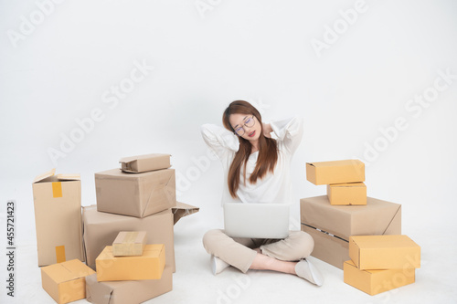 Small business entrepreneur or asian business woman sitting and packing parcels boxes on floor isolated on grey background. Concept online marketing. © waragron