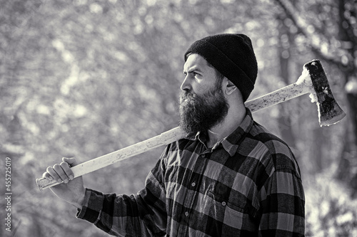 Lumberjack in the woods with an ax. Bearded man in hat with a hatchet. Handsome man, hipster. Lumberjack brutal bearded man with beard and moustache on winter day, snowy forest. Black and white