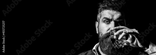 Sommelier tastes drink. Man holding a glass of whisky. Sipping whiskey. Portrait of man with thick beard. Macho drinking. Degustation, tasting. Black and white