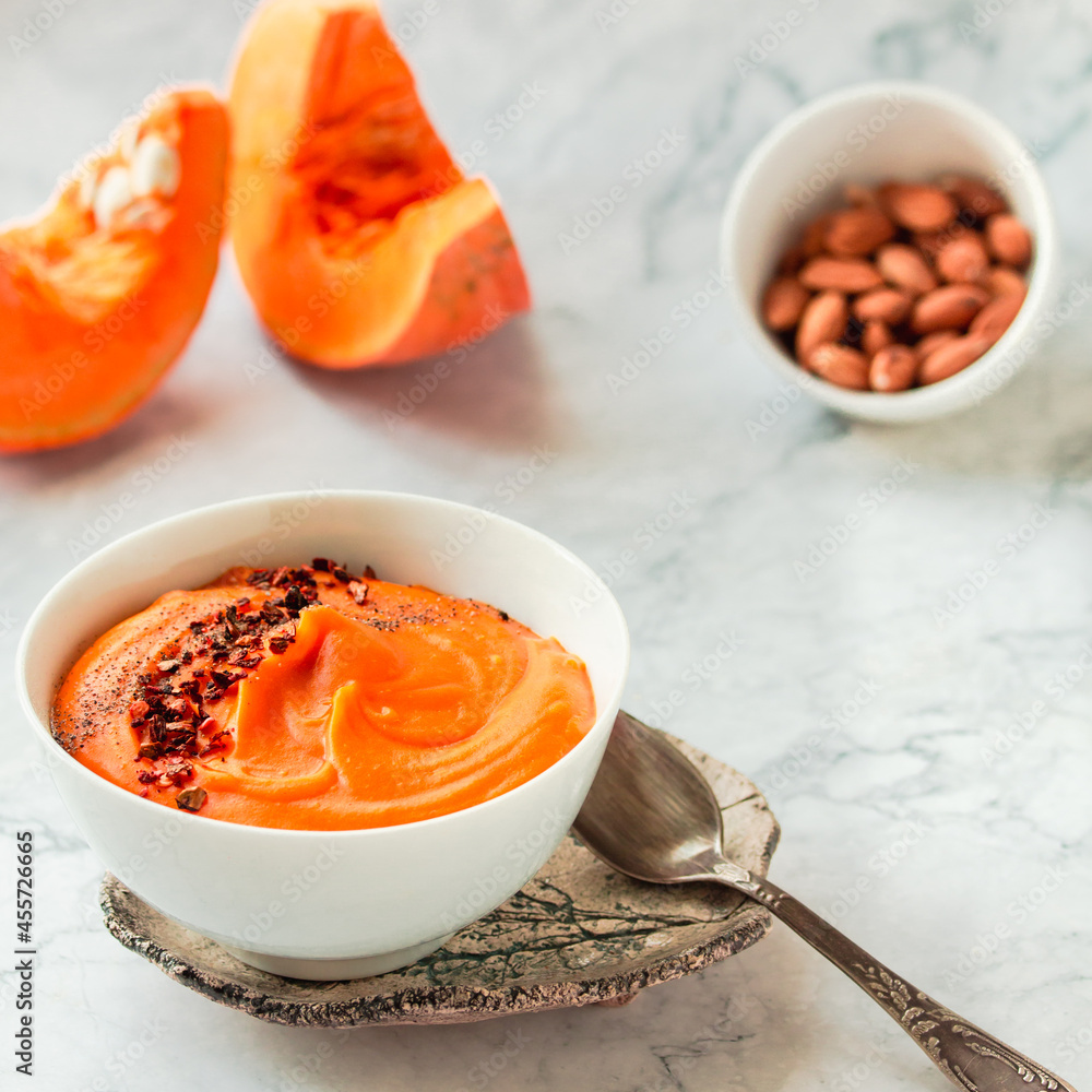 Tasty appetizing pumpkin creamy soup decorated with chili flakes pepper served in white bowl on marble background. Selective focus Tasty appetizing pumpkin creamy soup decorated with chili flakes pepper served in white bowl on marble background. Selective focus