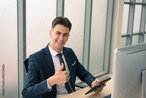 Adult smart business man in suit outfit sitting and working on tablet with happy and smile in modern office