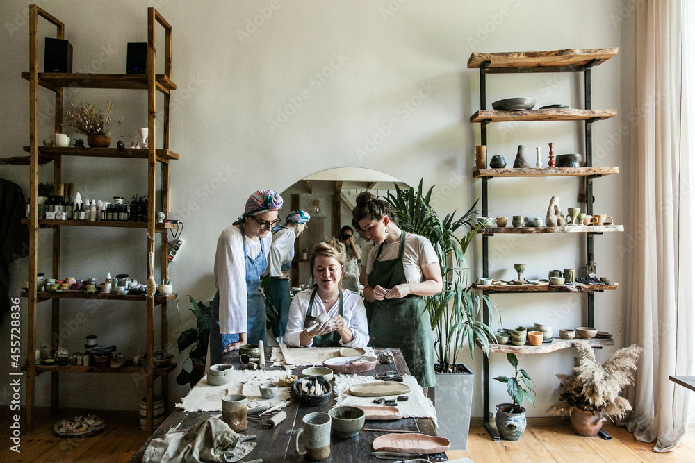 Three young girls in a ceramic workshop making dishes, daylight, general shot, side view, full-length