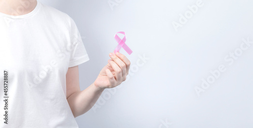 World Breast cancer day concept. Woman in white T-shirt holds pink ribbon in her hand. October Breast Cancer Awareness month. Copy space
