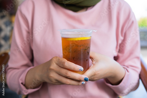 a cup of lemon tea ice is on the hand. a girl holds a tasty beverage in her hand. a kind of enjoying leisure time.