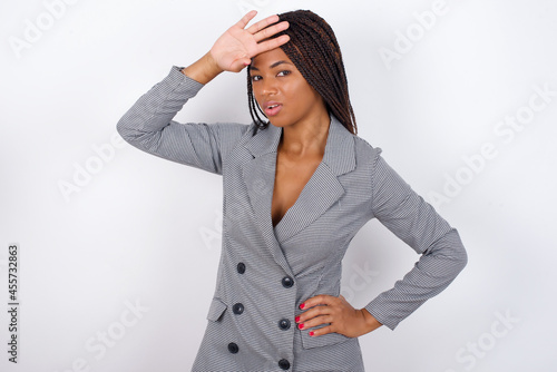 Young african american business woman with braids over white wall wiping forehead with hand making phew gesture, expressing relief feels happy that he prevented huge disaster. It was close enough photo