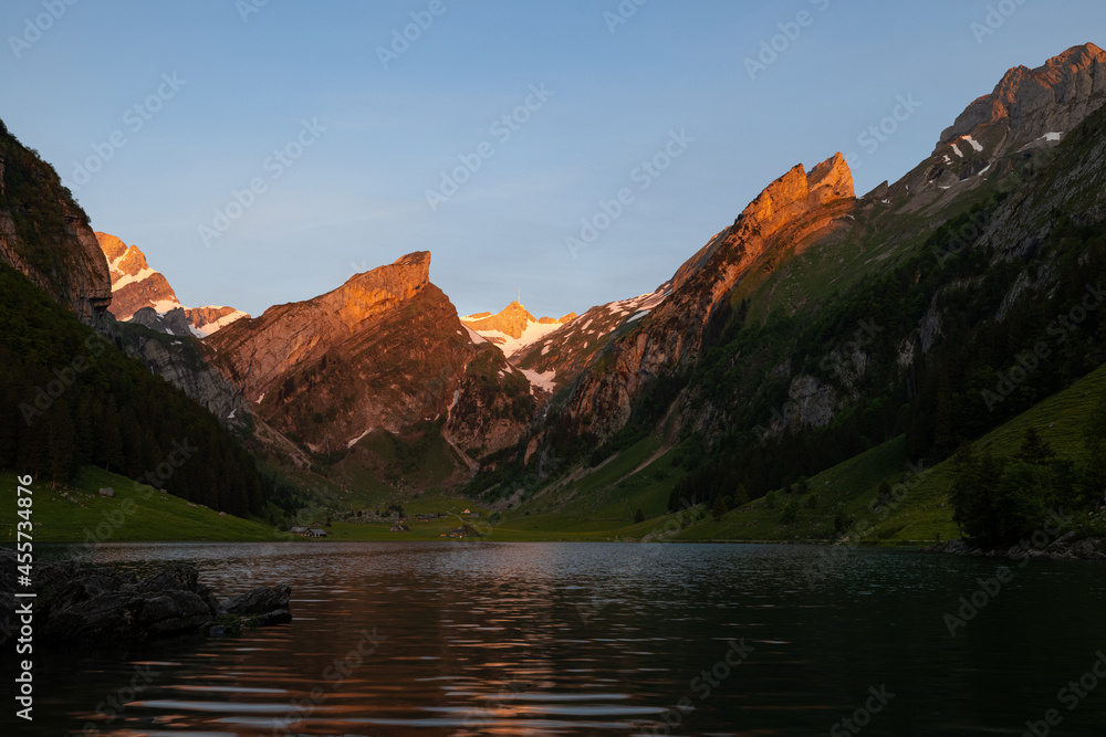 Epic sunrise by an alpine lake in Switzerland called Seealpsee. The sun shines to the peak of the mountain on the other side of the lake. This looks so wonderful.