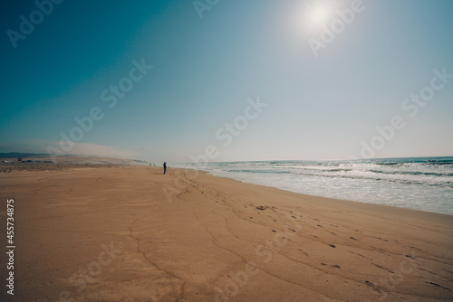 Sunny day on the beach, beautiful seascape background. Turquoise colored sea, wide sandy beach, silhouette of walking people on a horizon