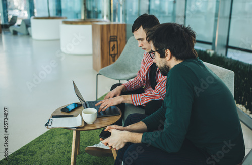 Focused young coworkers using laptop while sitting in contemporary offiice photo