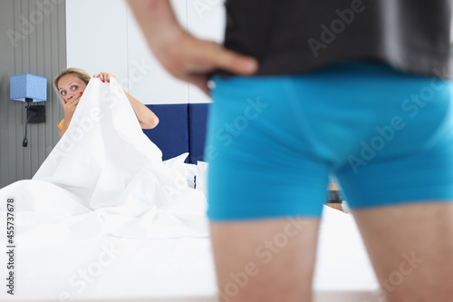 Frightened woman in bed looks at man in bedroom