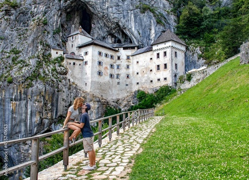 Woman and man kissing on brown wooden fence near Predjama Castle photo