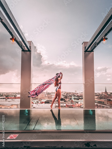 woman in monokini standing near clear glass fence beside swimming pool on rooftop of skyscraper photo
