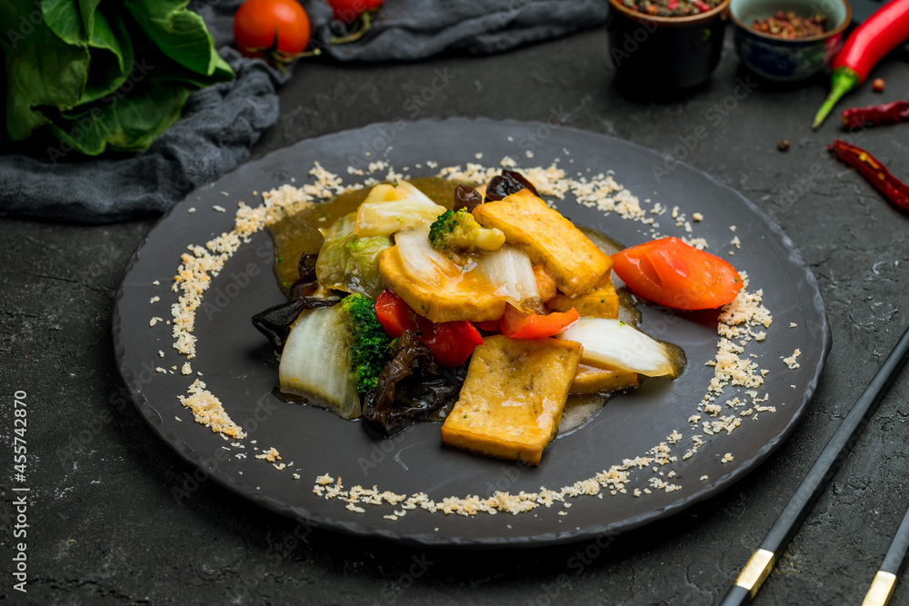 fried tofu with vegetables on plate on dark stone table
