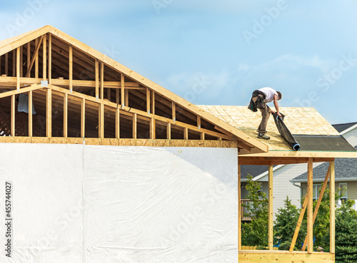 Worker installing underlayment sheet on wooden roof of new house. Renovation, improvement for exterior residential by professional builder. Durable build and construction business. Labor job concept photo