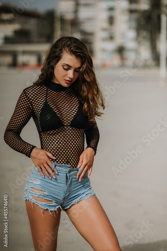 Fotografie Fitness model posing on the beach in blue jeans shorts and sexy black body