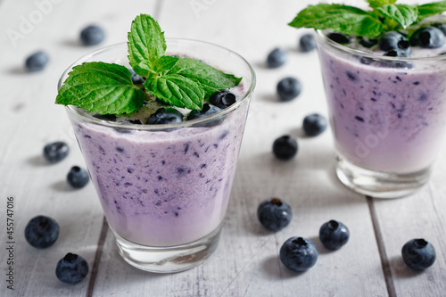 Blueberry smoothie with milk and mint in a glass, on rustic wooden table.