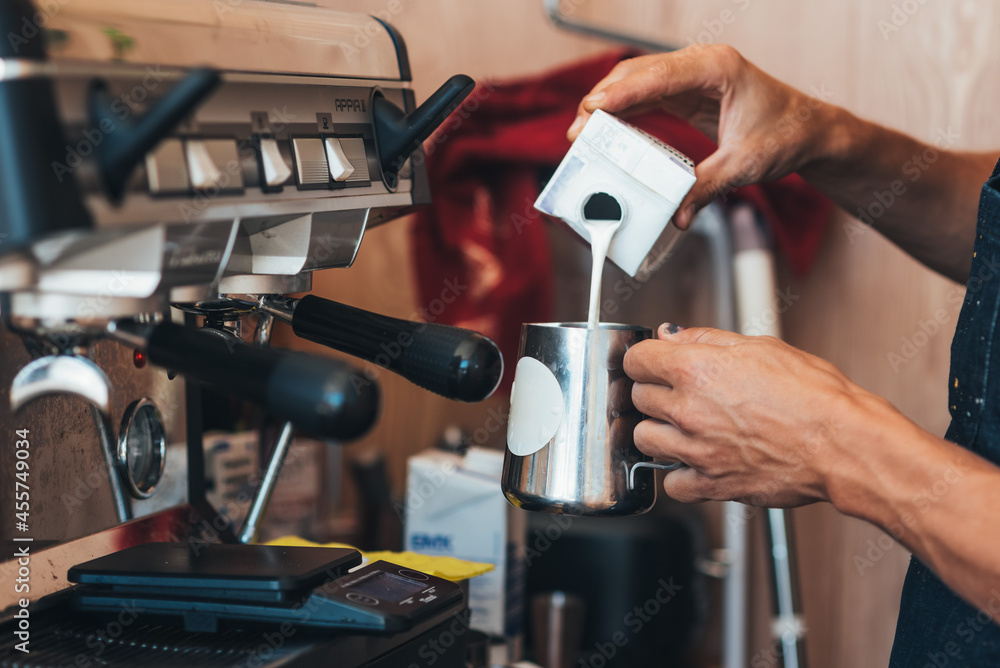 the barista pours milk from a tin can into coffee in a paper disposable cup the barista pours milk from a tin can into coffee in a paper disposable cup