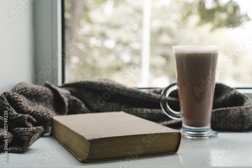 Cocoa drink, warm knitted scarf and old book on white windowsill. Hot chocolate.