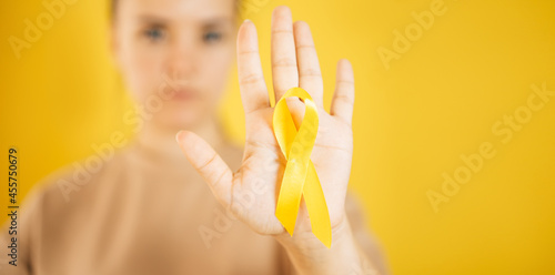 a woman holding a yellow gold ribbon in her hand on a yellow background, Bone cancer, awareness of childhood cancer, yellow September, the concept of World Suicide Prevention Day