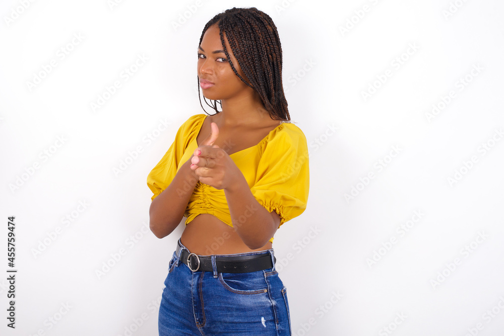 Hey you, bang. Joyful and charismatic good-looking Young african american woman with braids over white wall winking and pointing with finger pistols at camera happily and cheeky. Hey you, bang. Joyful and charismatic good-looking Young african american woman with braids over white wall winking and pointing with finger pistols at camera happily and cheeky.