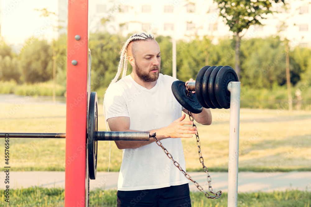 A man with a beard and braid hair prepares for a barbell press and lifts discs with weights. A man with a beard and braid hair prepares for a barbell press and lifts discs with weights.