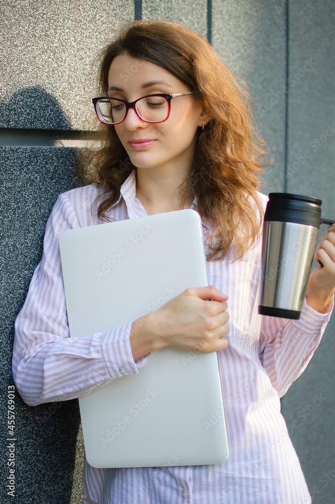 Female portrait of young woman with silver laptop and cup of coffee waiting for a meeting near dark grey wall in the morning, remote job, coffeebreak, smart student concept Female portrait of young woman with silver laptop and cup of coffee waiting for a meeting near dark grey wall in the morning, remote job, coffeebreak, smart student concept
