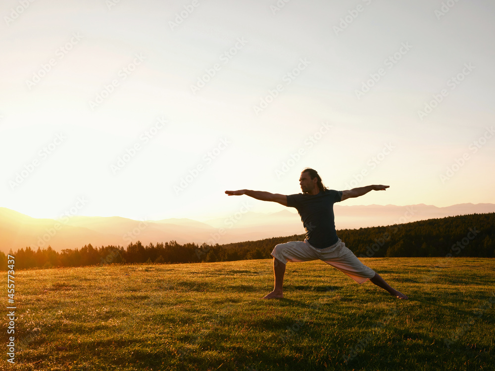 Man practicing Virabhadrasana on lawn in sunrise Man practicing Virabhadrasana on lawn in sunrise