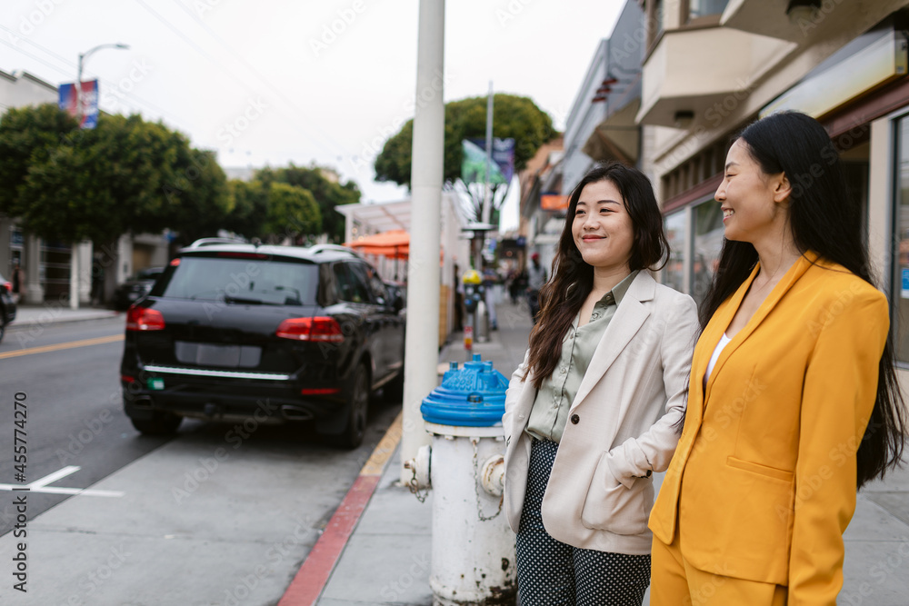 Cheerful Chinese girlfriends standing on sidewalk Cheerful Chinese girlfriends standing on sidewalk