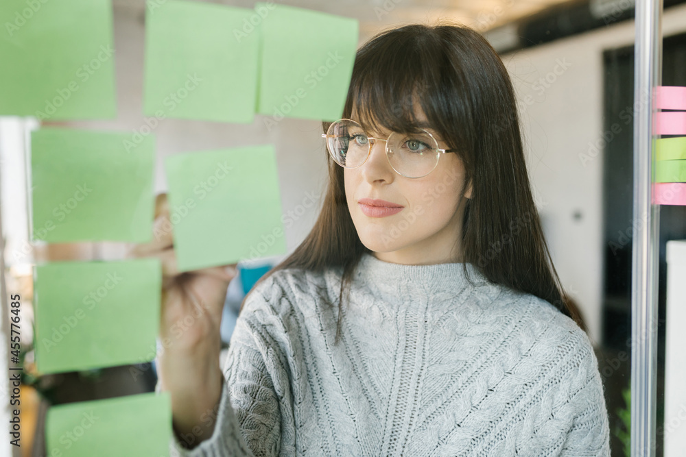 © Mihajlo Ckovric/Stocksy - Young woman writing notes on a stickers on a glass wall © Mihajlo Ckovric/Stocksy - Young woman writing notes on a stickers on a glass wall