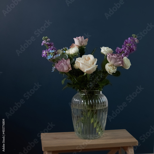 Bouquet of hackelia velutina, purple and white roses, small tea roses, matthiola incana and blue iris in glass vase . Dark blue wall photo