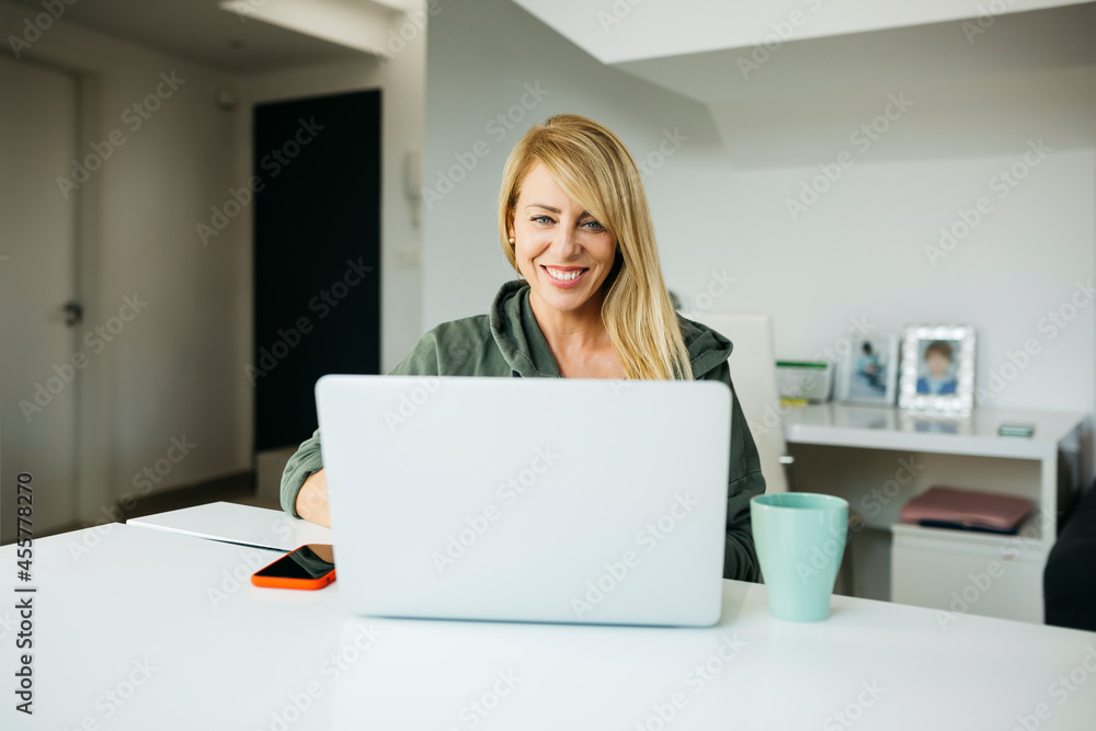 Middle age smiling blonde woman using a laptop in a livingroom Middle age smiling blonde woman using a laptop in a livingroom