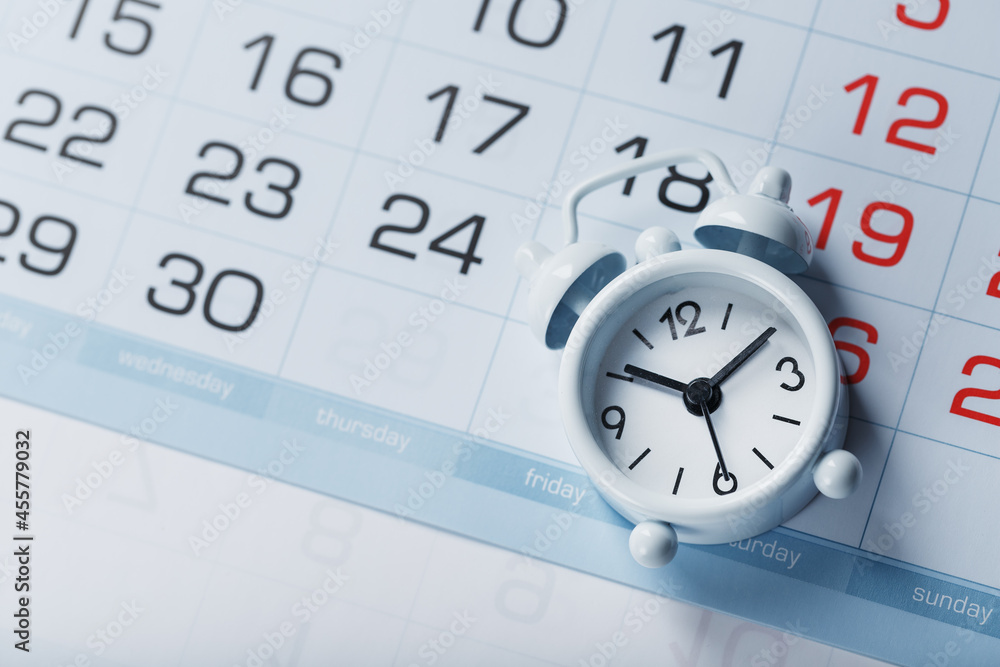 Time on a white alarm clock lying on the calendar and a blue background. Time on a white alarm clock lying on the calendar and a blue background.
