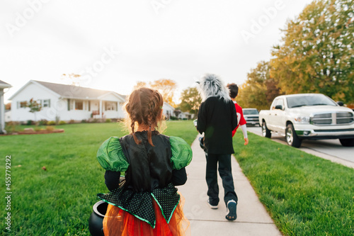 The backside of children walking down the sidewalk in cosutmes.  photo