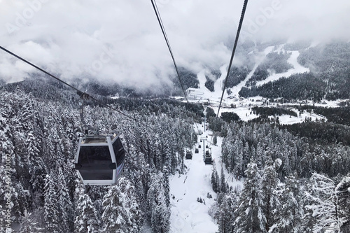 Gondola lift goes up along the slope at the winter ski resort in the forest. Fog im mountains on background, winter sports concept