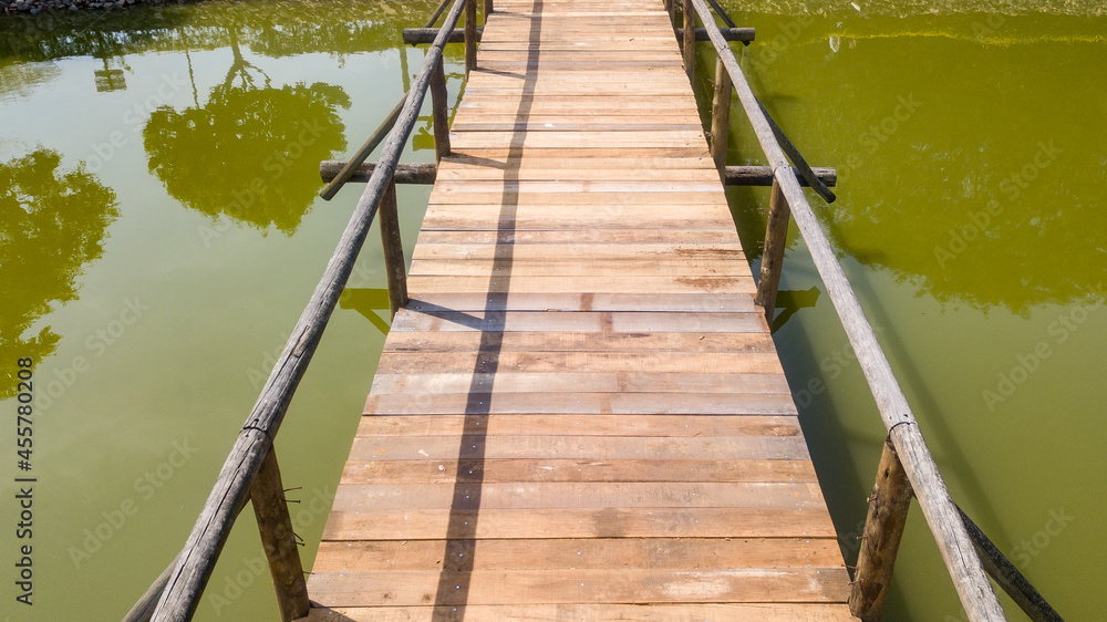 Wooden bridge, with handrail, in a lake with greenish water, in drone image
