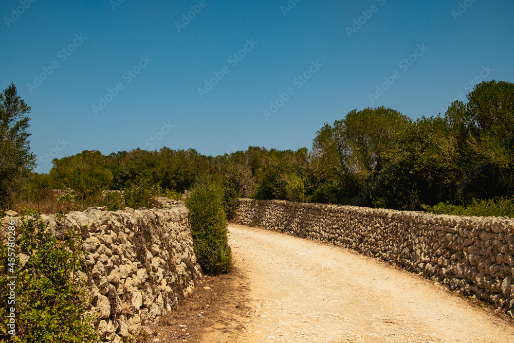 spanish unpaved street in the spanish countryside with stones sides. an old empty dirt road is seen on summer day with clear blue sky, off the beaten path