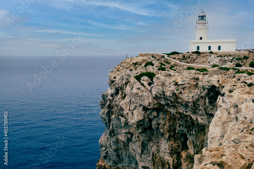 Menorca, Spain View of Cavalleria lighthouse with rocky cliff during a summer day with dramatic cloudy sunset in the balearic island of Menorca in Spain