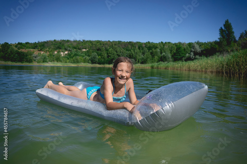 A little cute girl in a swimsuit swims on an inflatable mattress on a blue career lake.