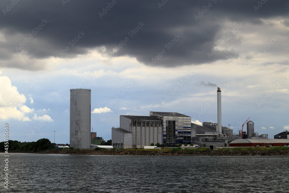 Industry by the water. Factory. Great and beautiful view in a far distance. Gray dark clouds in the sky. Copy space for extra text. At the Swedish lake Vänern or Vanern. Lidköping, Sweden, Europe.