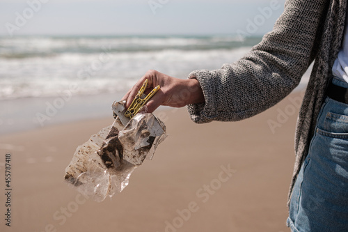 Faceless young woman cleaning the beach of plastics photo