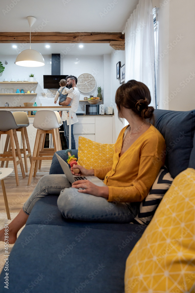 Woman working on laptop at home with man and child Woman working on laptop at home with man and child