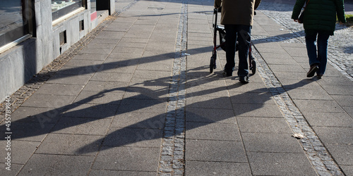long shadows of two elderly people on the pavement of the sidewalk, man walking with a walking aid