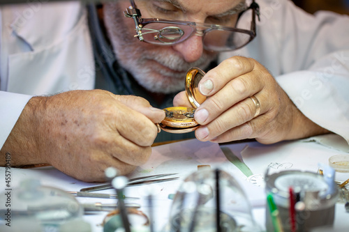 Fotografie Mature Watchmaker repairing vintage pocket watch and clock on the workbench