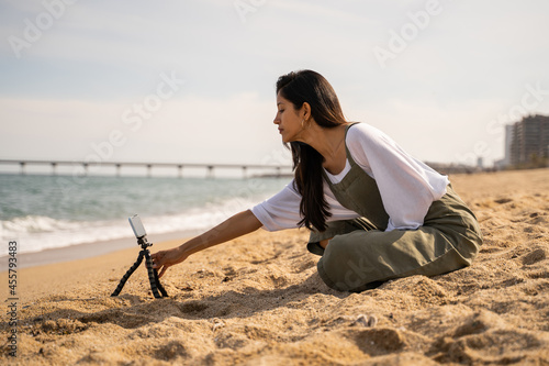 Beautiful young woman filming meditation video at beach photo